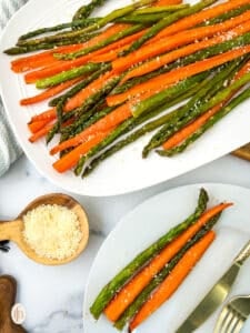 A plate of roasted carrots and asparagus with a wooden spoon and a plate.