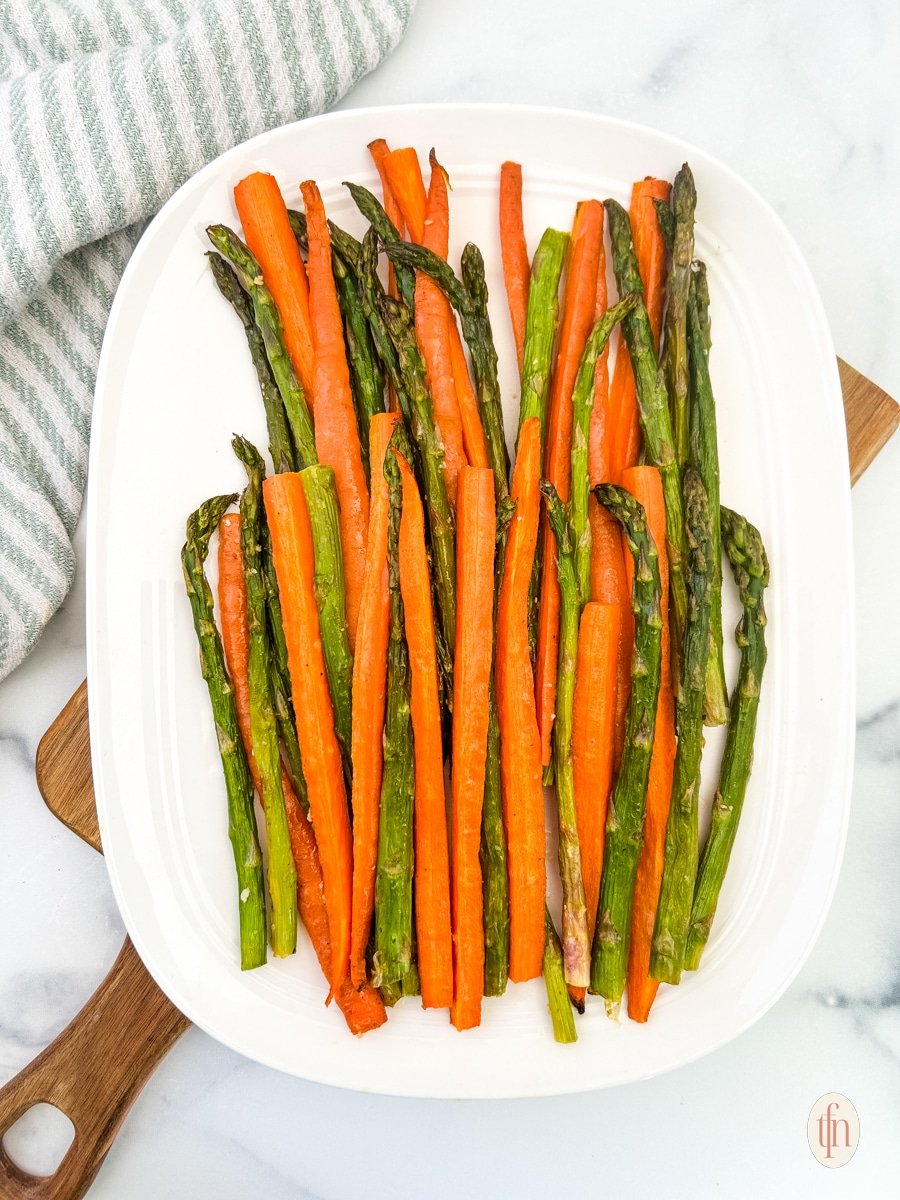 A plate of roasted carrots and asparagus on top of a wooden board.