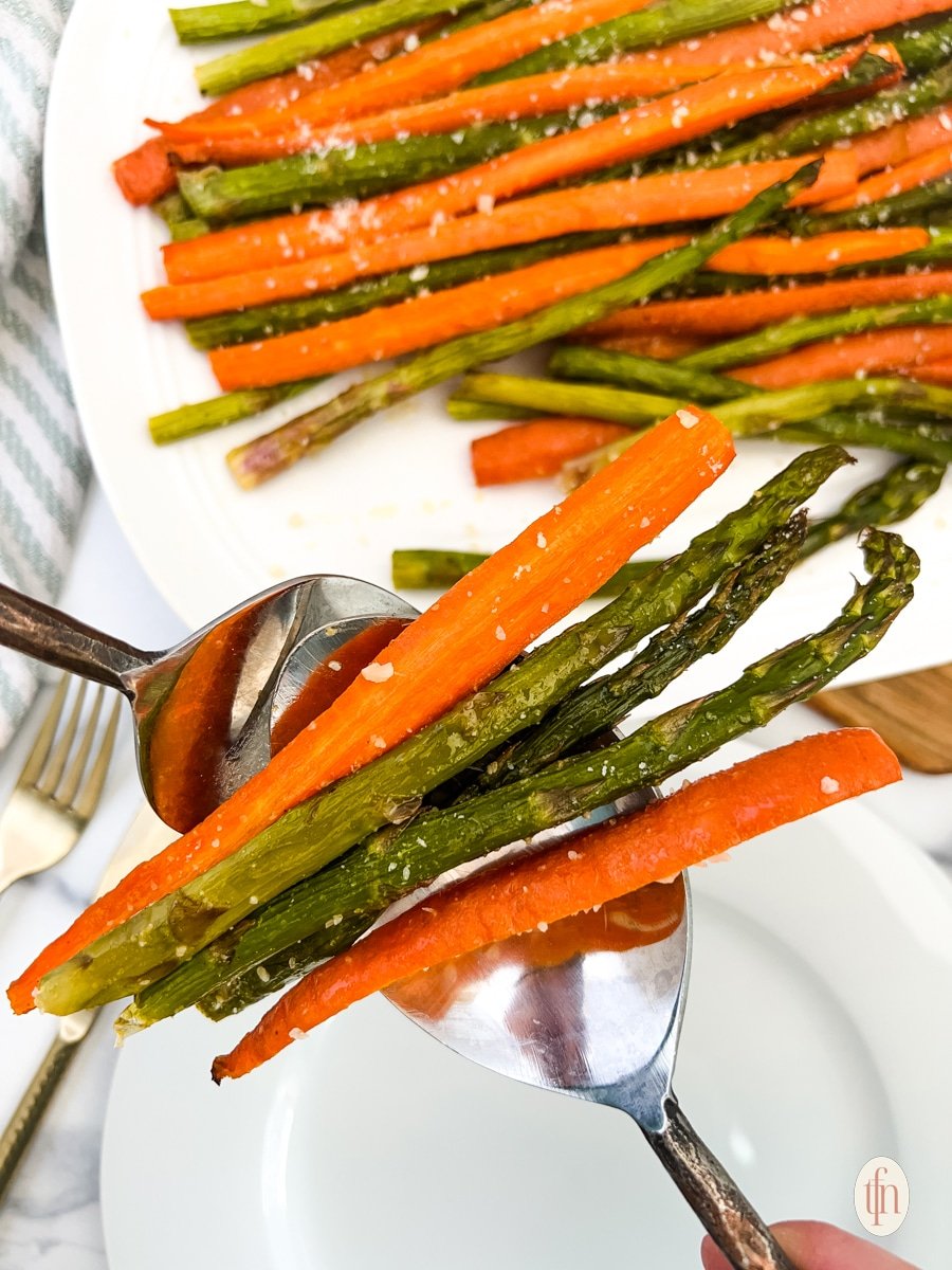 Getting roasted carrots and asparagus using two spoons.