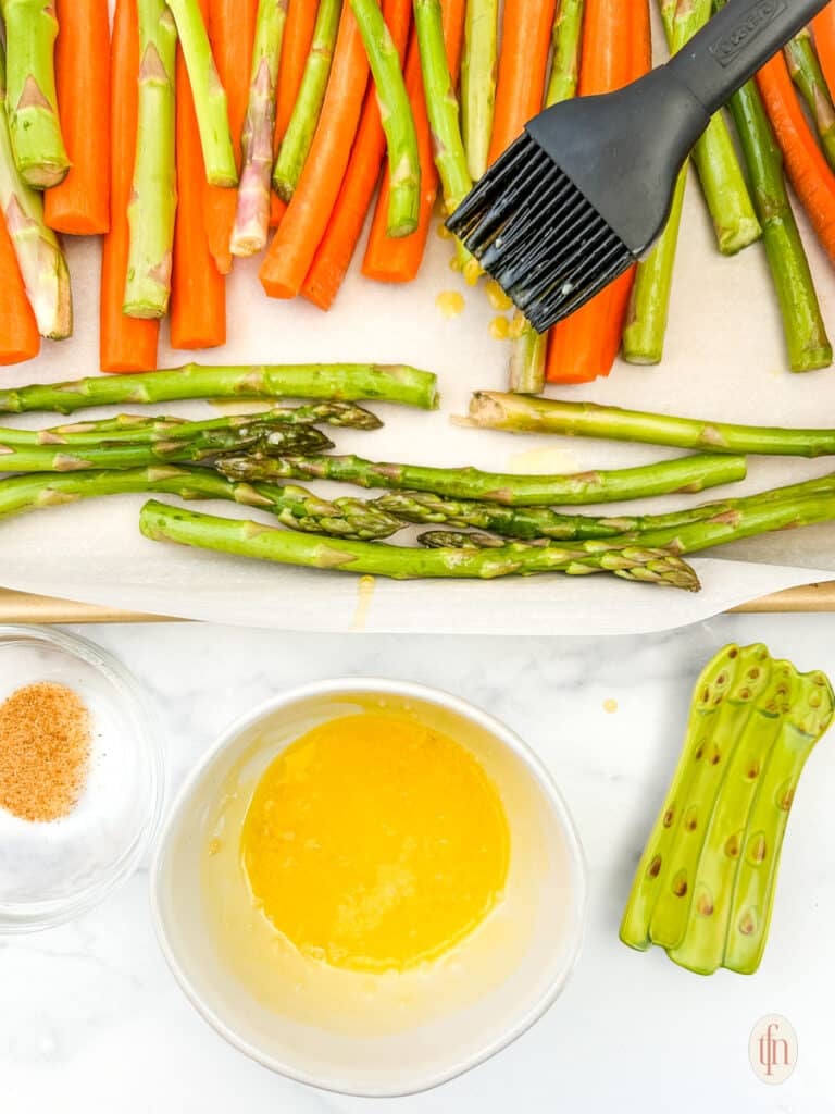 Brushing the carrots and asparagus with butter using a pastry brush.