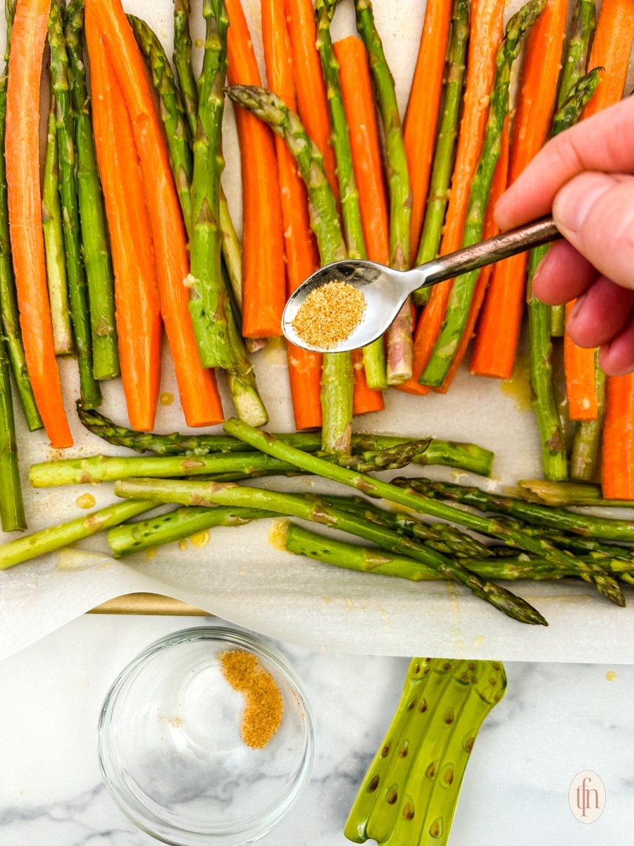 Adding seasoning to a plate of raw carrots and asparagus.