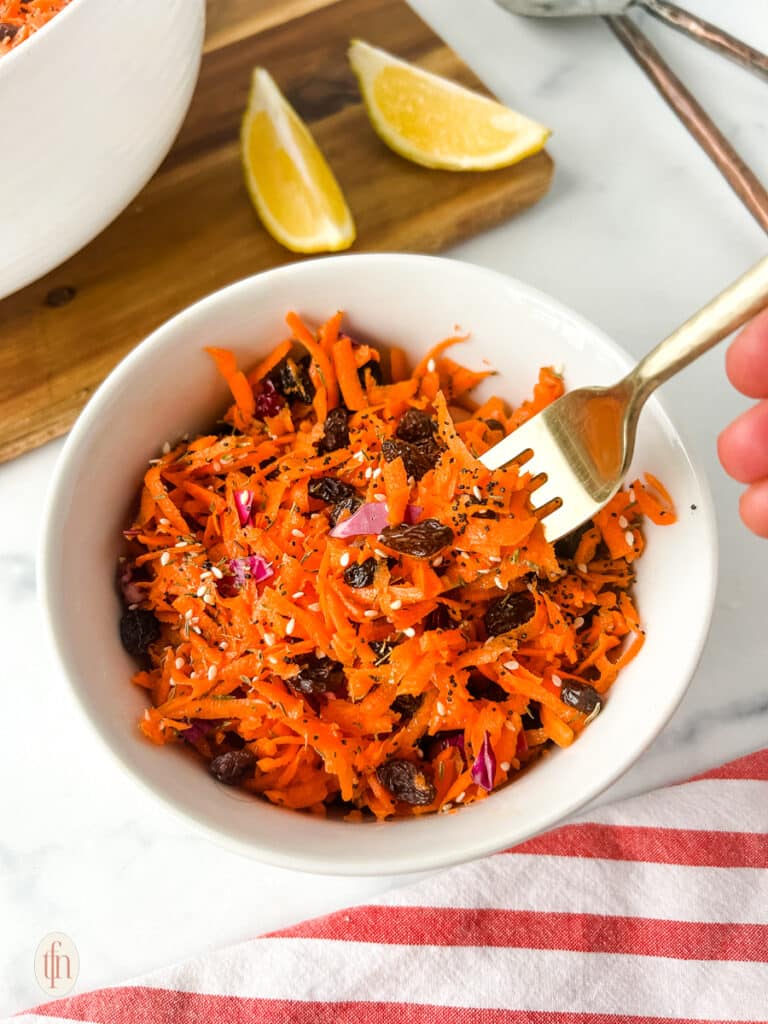 Shredded carrot in a white bowl with fork.