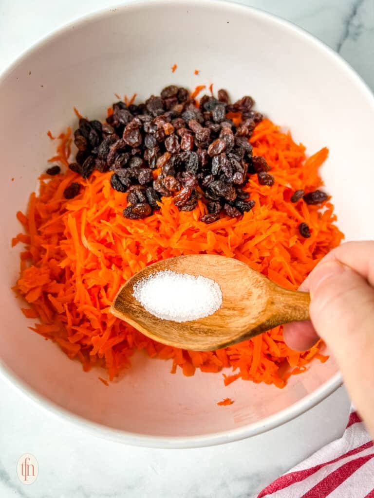 Adding ingredients to the mixing bowl to make shredded carrots salad.