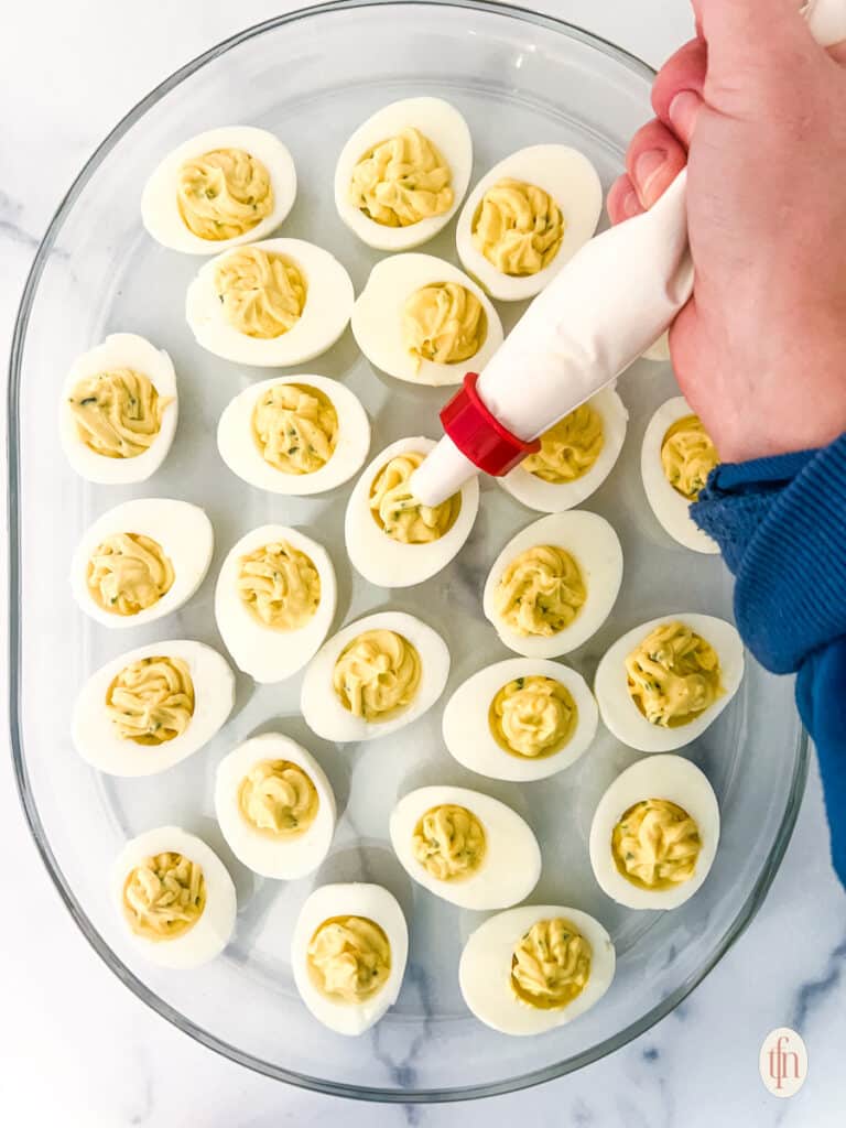 Egg yolk mixture being piped onto the sliced boiled eggs to make spicy deviled eggs.