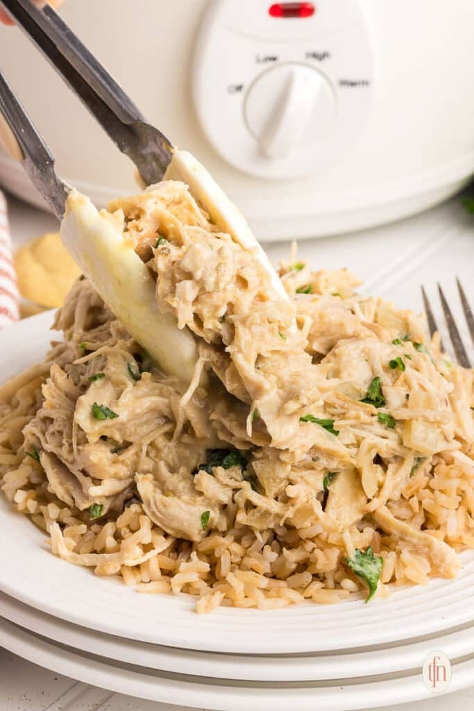 Serving crockpot honey garlic chicken with tongs.