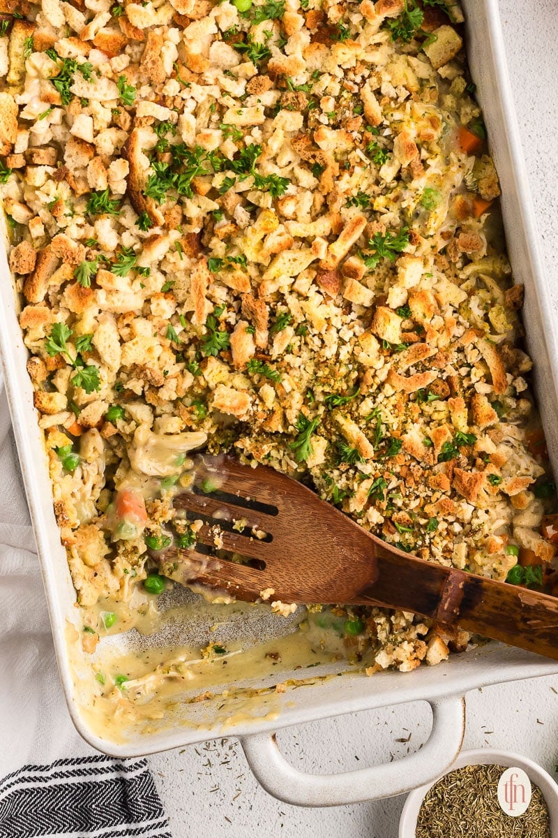 Chicken casserole with stove top stuffing with wooden spoon in a baking dish.