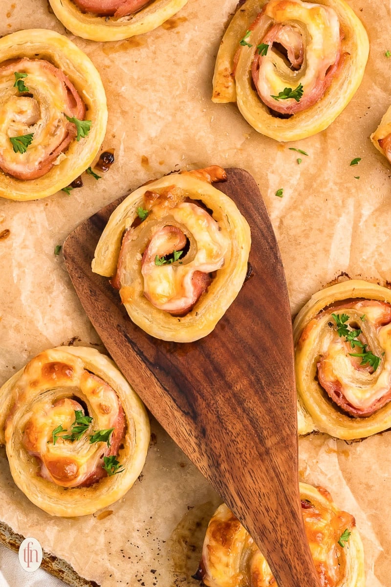 Ham and cheese pinwheels on a top of a baking sheet with parchment paper.