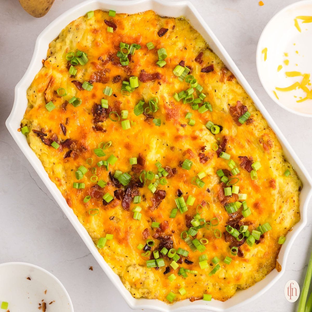 a casserole dish of baked mashed potatoes topped with bacon and green onions.