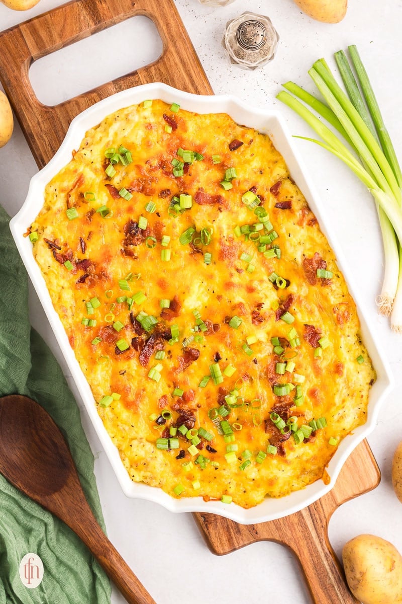 A casserole dish of baked mashed potatoes recipe on top of a wooden board.