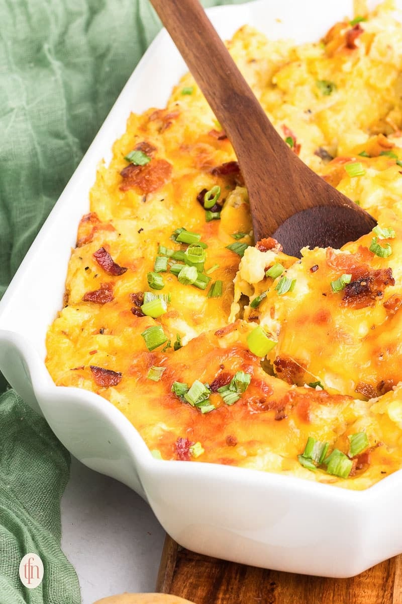Baked mashed potatoes in a casserole dish with a wooden spoon.