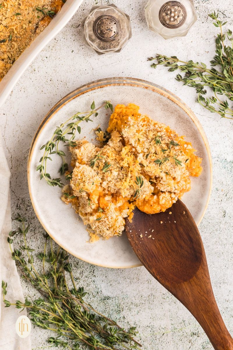 A scoop of canned sweet potato casserole on a plate with wooden spoon and fresh herbs.