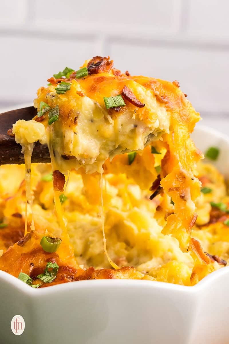 Scooping baked mashed potatoes using a wooden spoon.