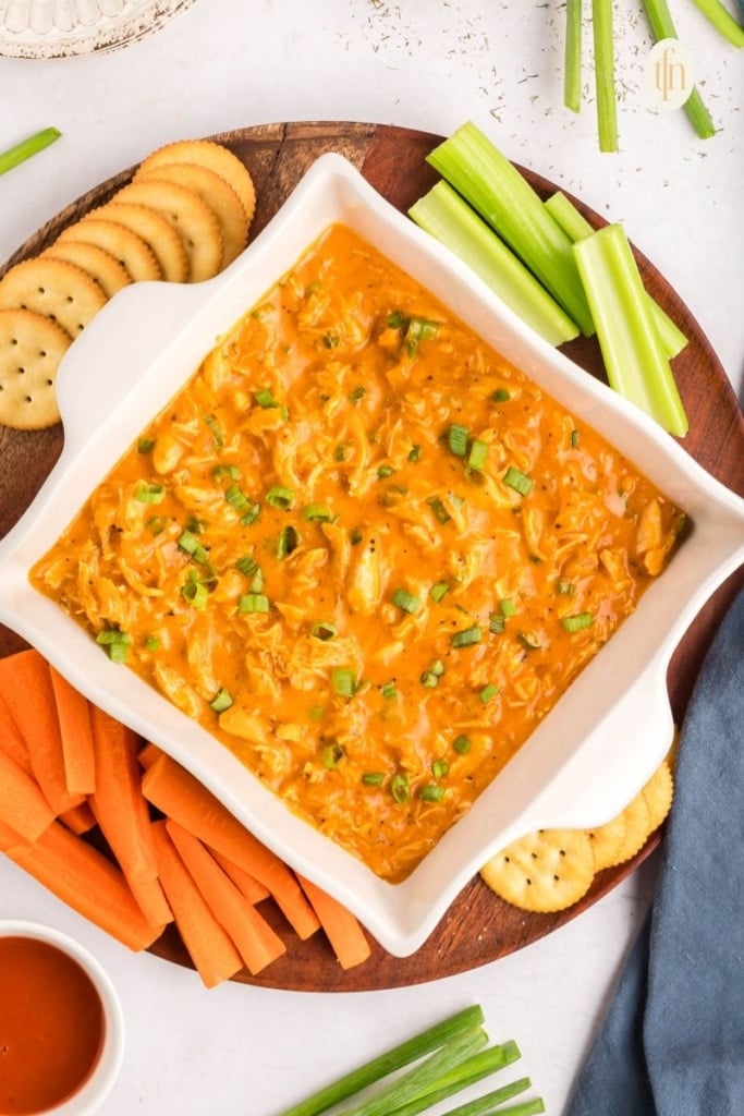 A serving of buffalo dip on a platter with crackers and vegetables.