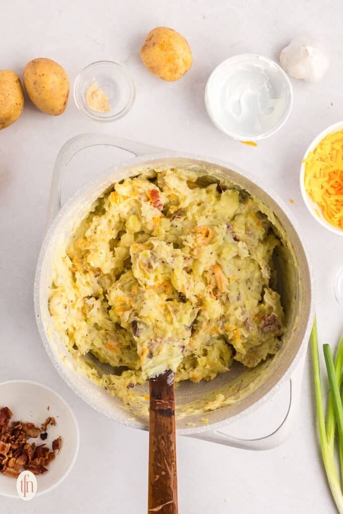 A mixture of mashed potatoes in a pot with a wooden spoon.