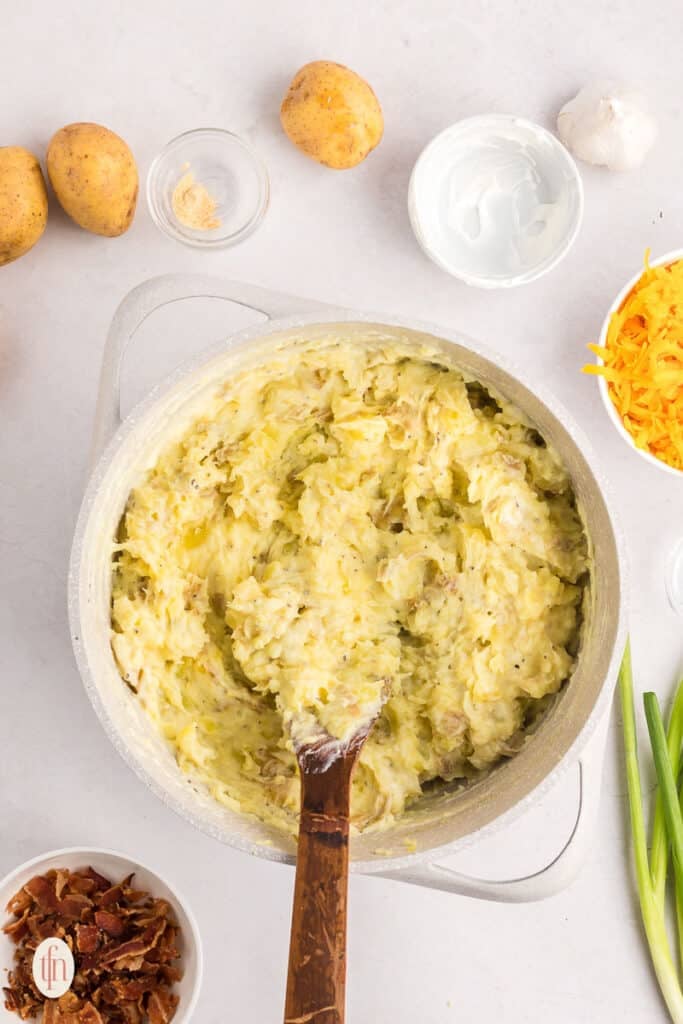 A mixture of mashed potatoes in a pot with a wooden spoon.