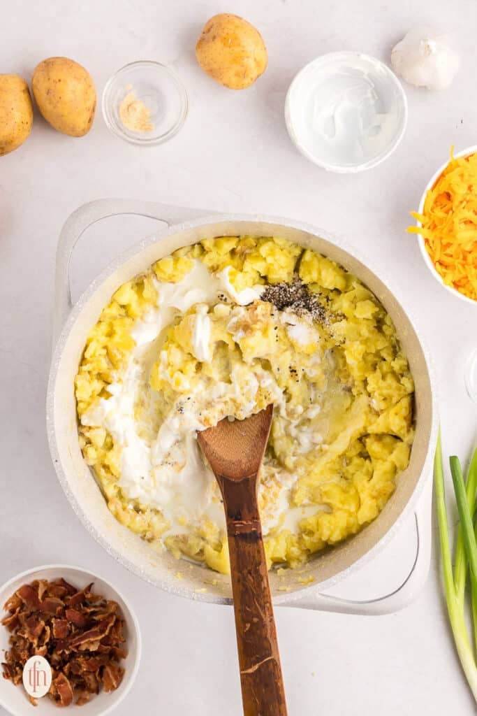 Mixed potatoes and milk in a pot with wooden spoon.