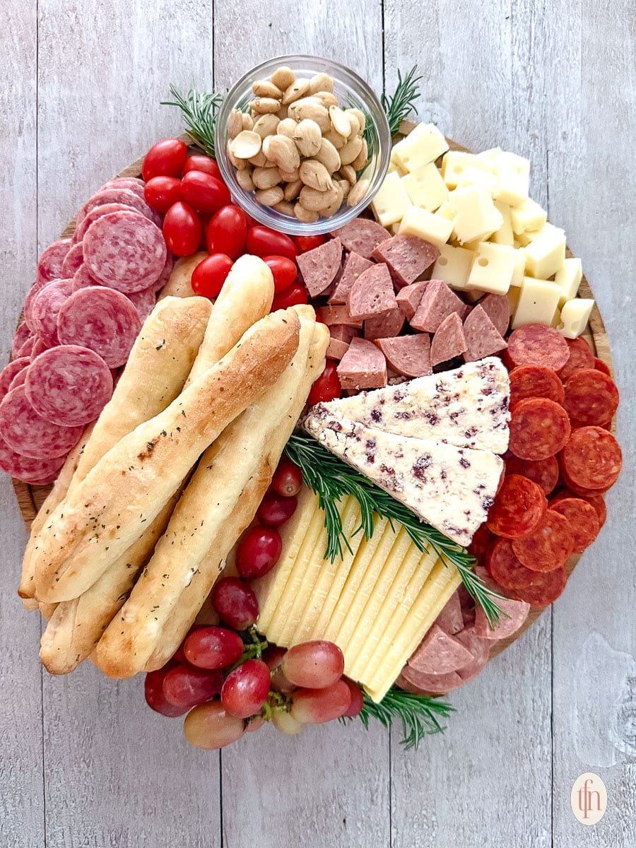 A round charcuterie board mixed with bread, meat, tomatoes, fruits, and cheese.