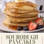 A vertical image with the title "SOURDOUGH PANCAKES with discard" at the bottom. The image is a close-up of a stack of fluffy sourdough pancakes topped with butter and syrup, garnished with berries. The website "TheFeatheredNester.com" is at the bottom.