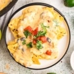 Nachos topped with cheese sauce and garnish on a round plate.