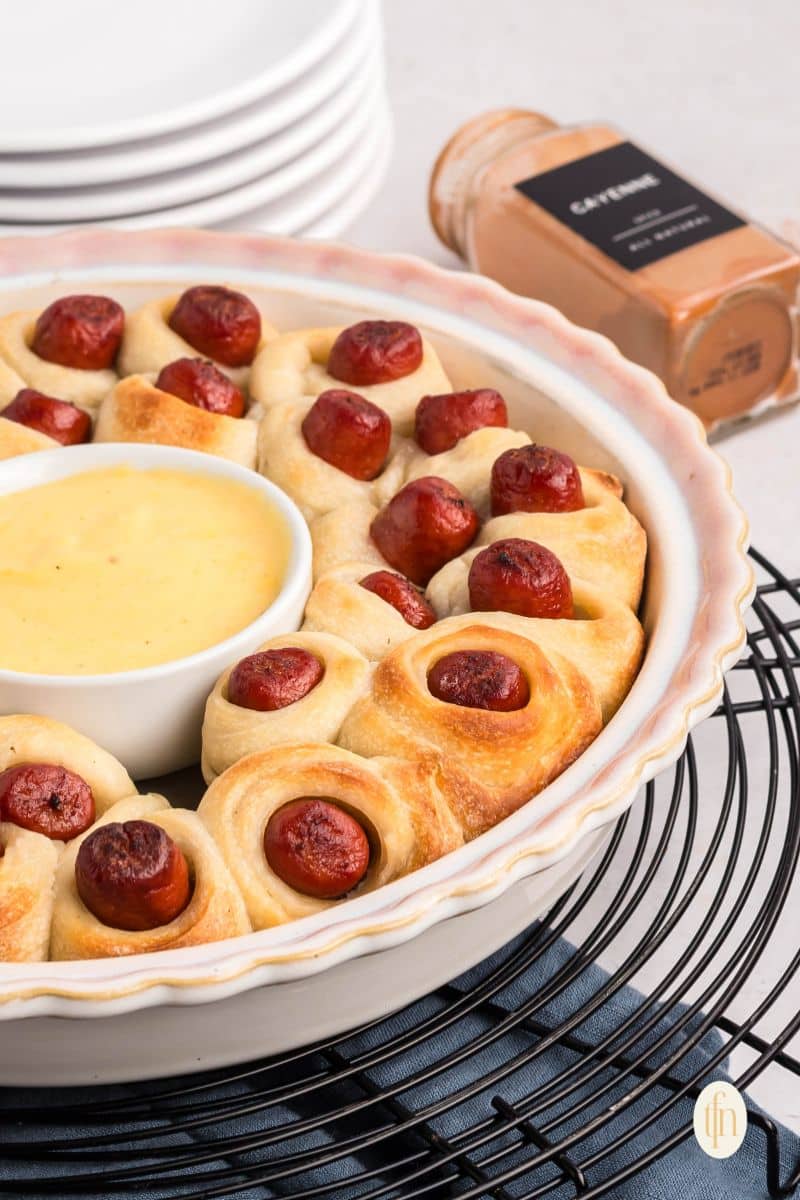 A round dish with pigs in a blanket and a bowl of sauce in the middle.