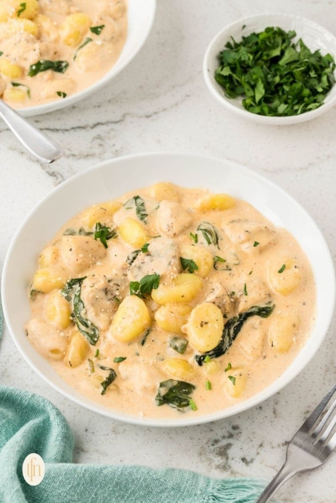 A bowl of chicken and gnocchi with sauce.