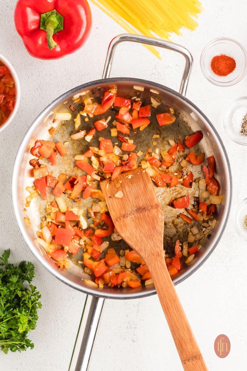 Sautéed ingredients in a skillet with wooden spoon.