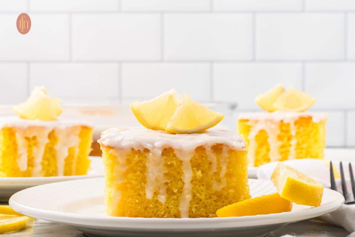 A slice of cake with white glaze and slice of lemon on top.