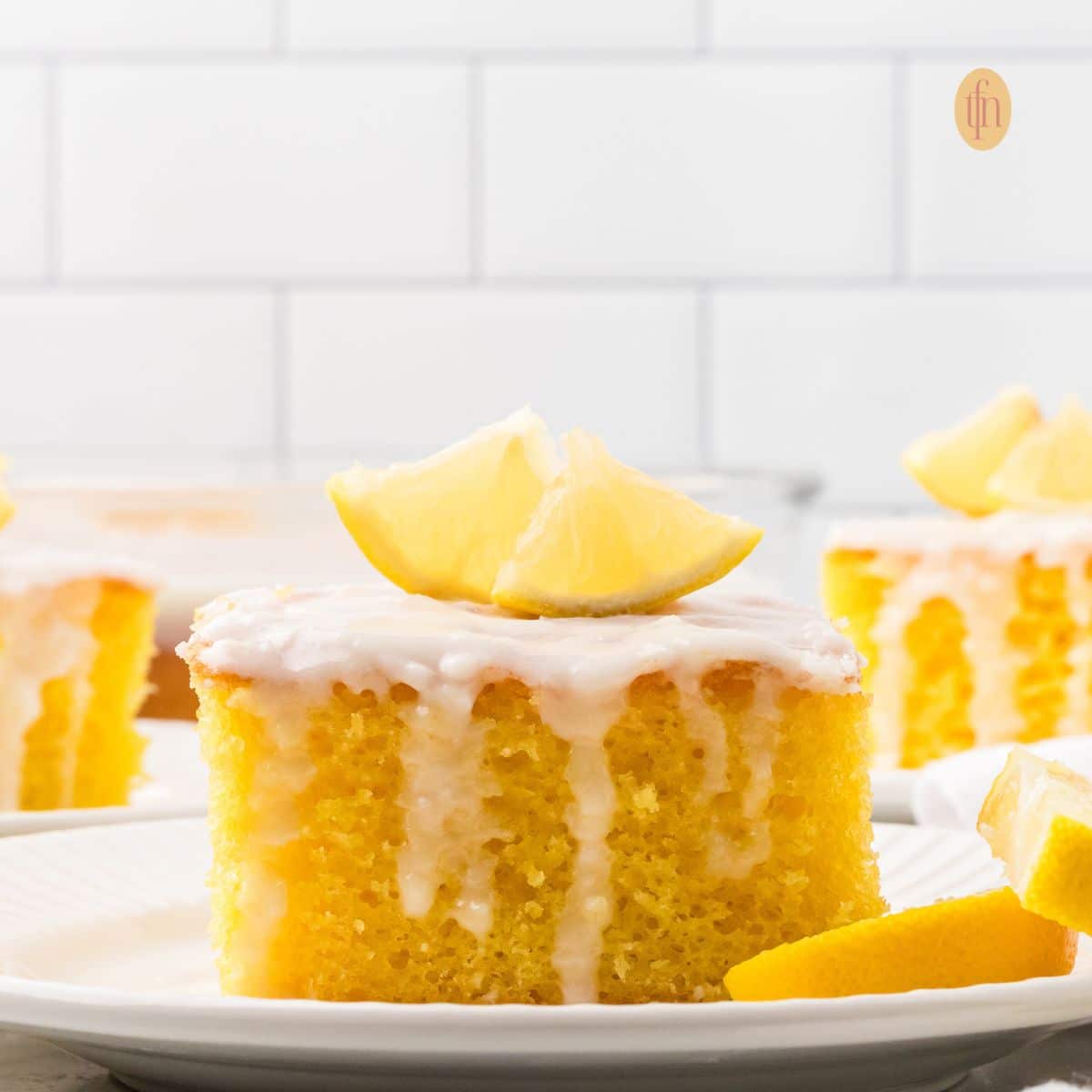 A slice of cake with white glaze and slice of lemon on top.