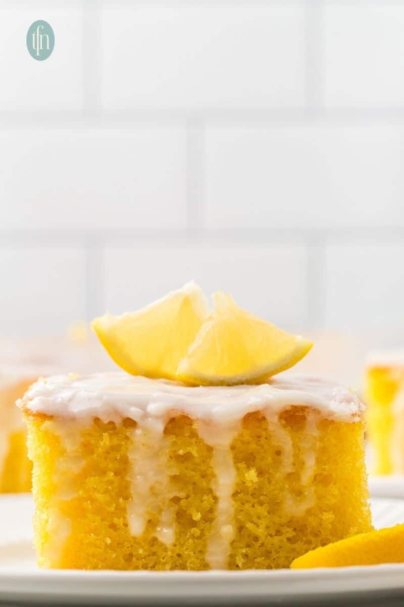 A slice of cake with white glaze and slice of lemon on top.