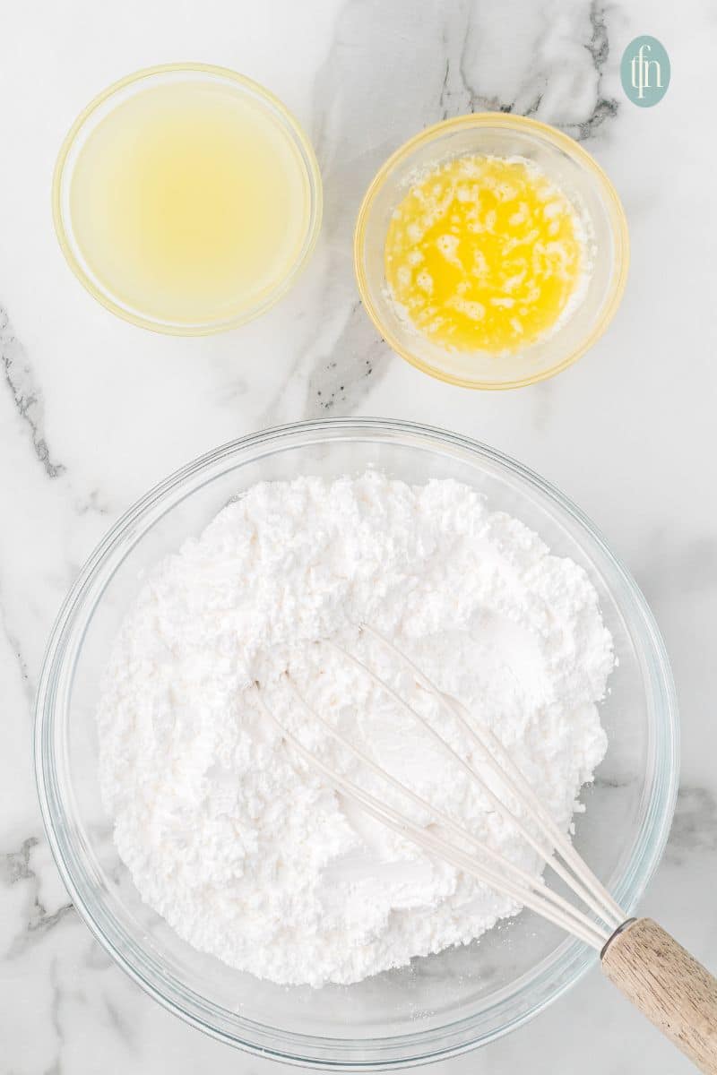 A bowl of powdered sugar with whisk and a bowl of lemon juice and butter.