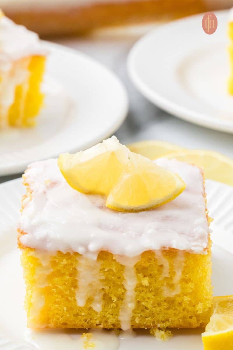 A slice of cake with white glaze and slice of lemon on top.