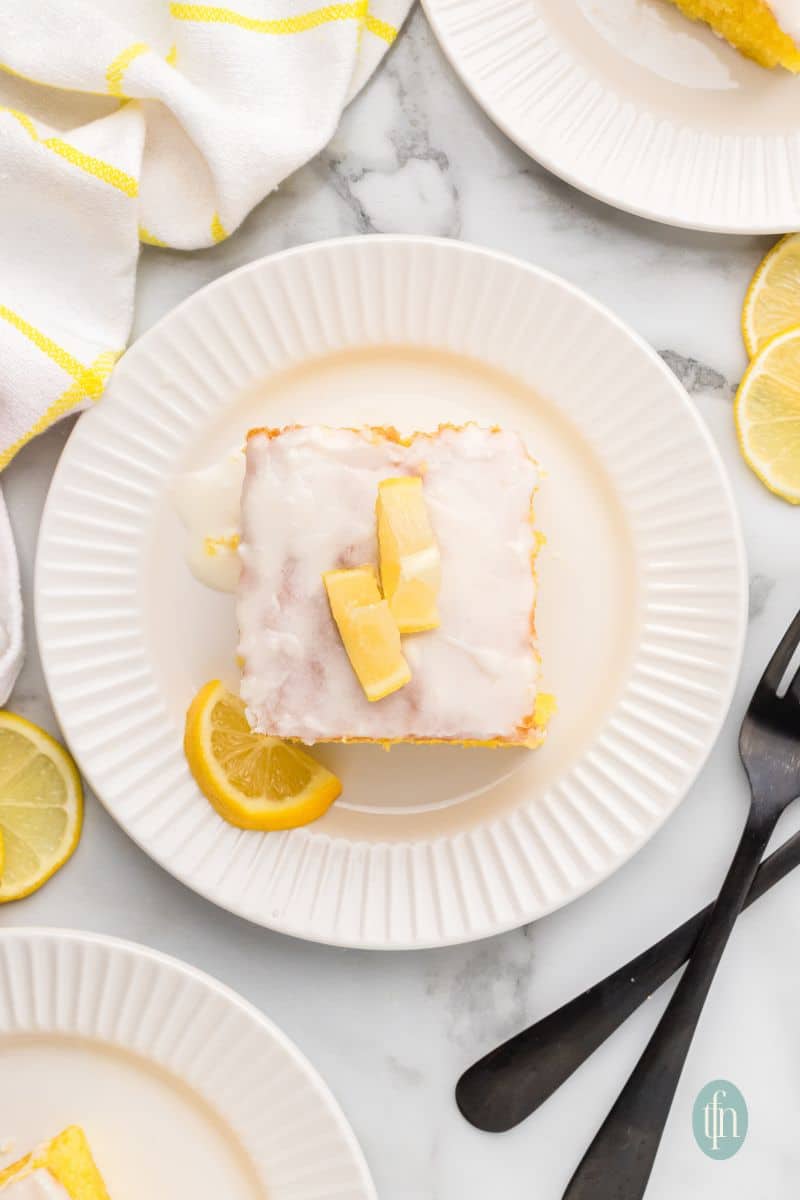 A slice of cake with white glaze and slice of lemon on top.