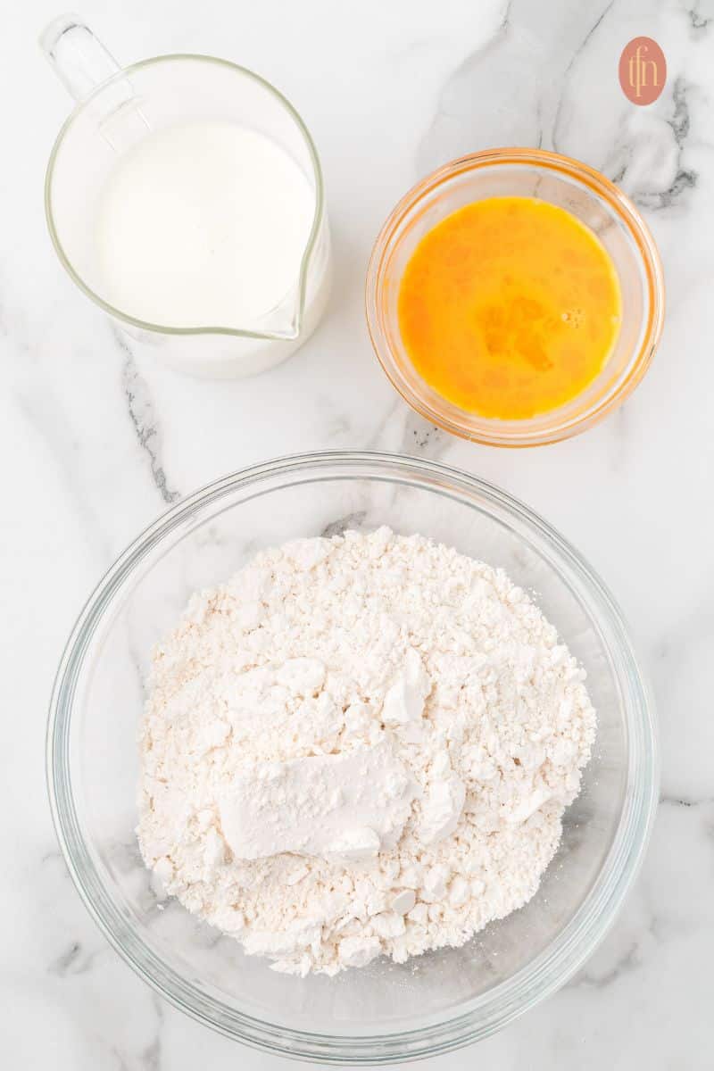 A bowl of flour mixture with a pitcher of milk and beaten eggs.