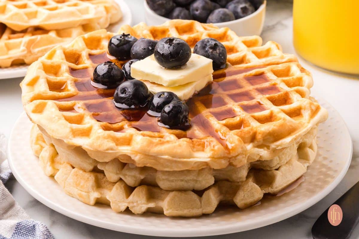 Stack of waffles with blueberries, syrup, and butter.