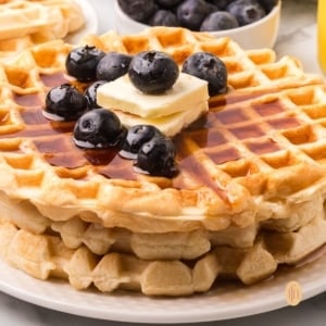 Stack of waffles with blueberries, syrup, and butter.