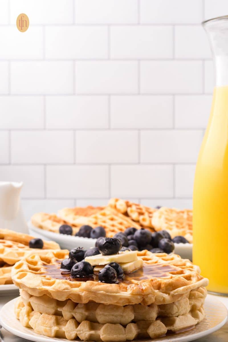 Stack of waffles with blueberries, syrup, and butter.