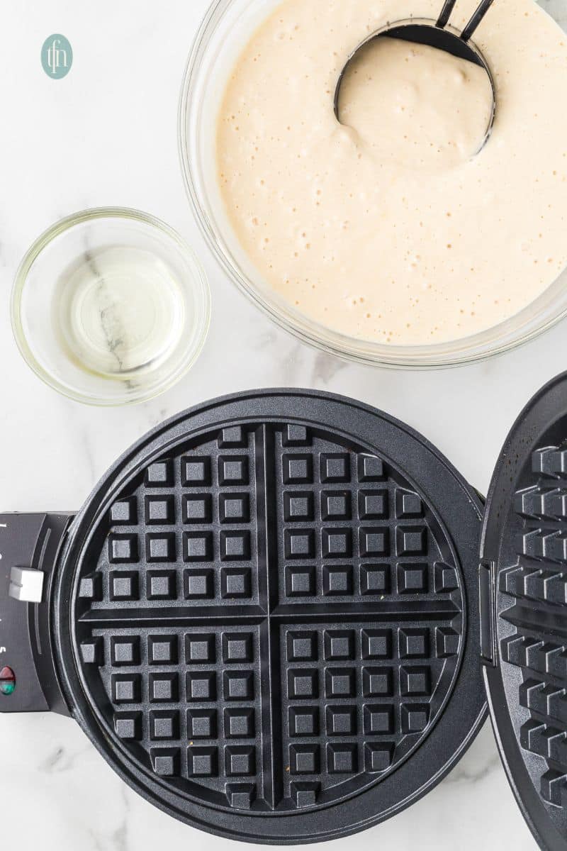 A waffle maker and a bowl of batter mixture.