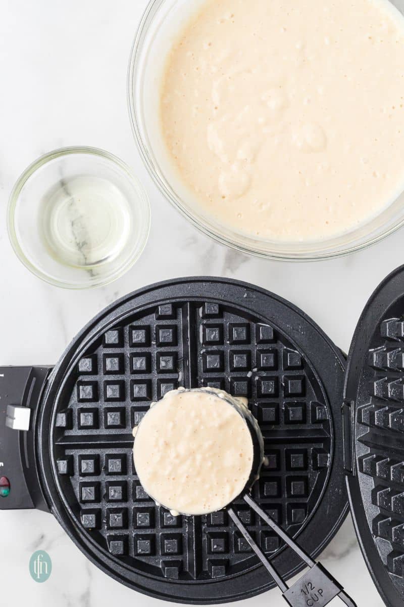 A waffle maker with a cup of batter.