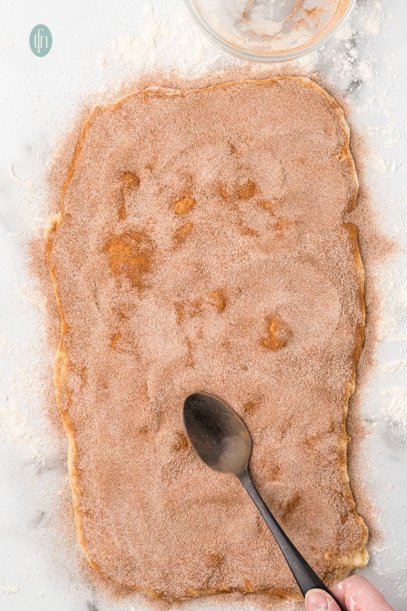 Flatten dough with brown powder on a counter top.
