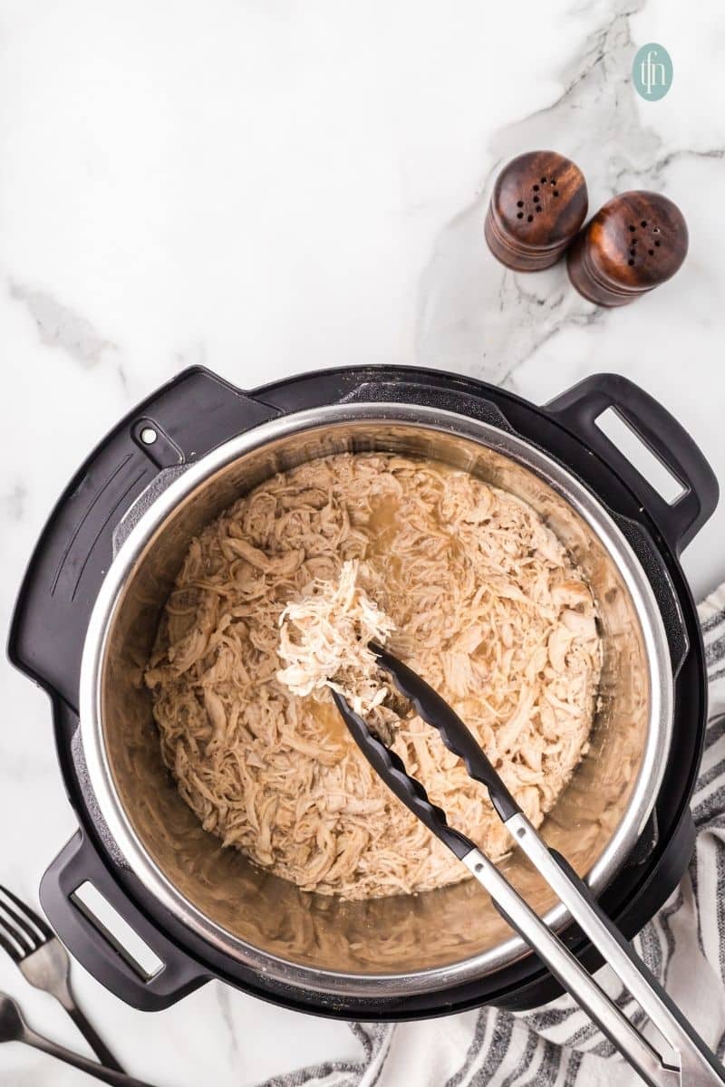 Shredded chicken in an Instant Pot with tong.
