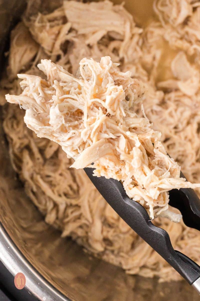 Shredded chicken in an Instant Pot with tong.