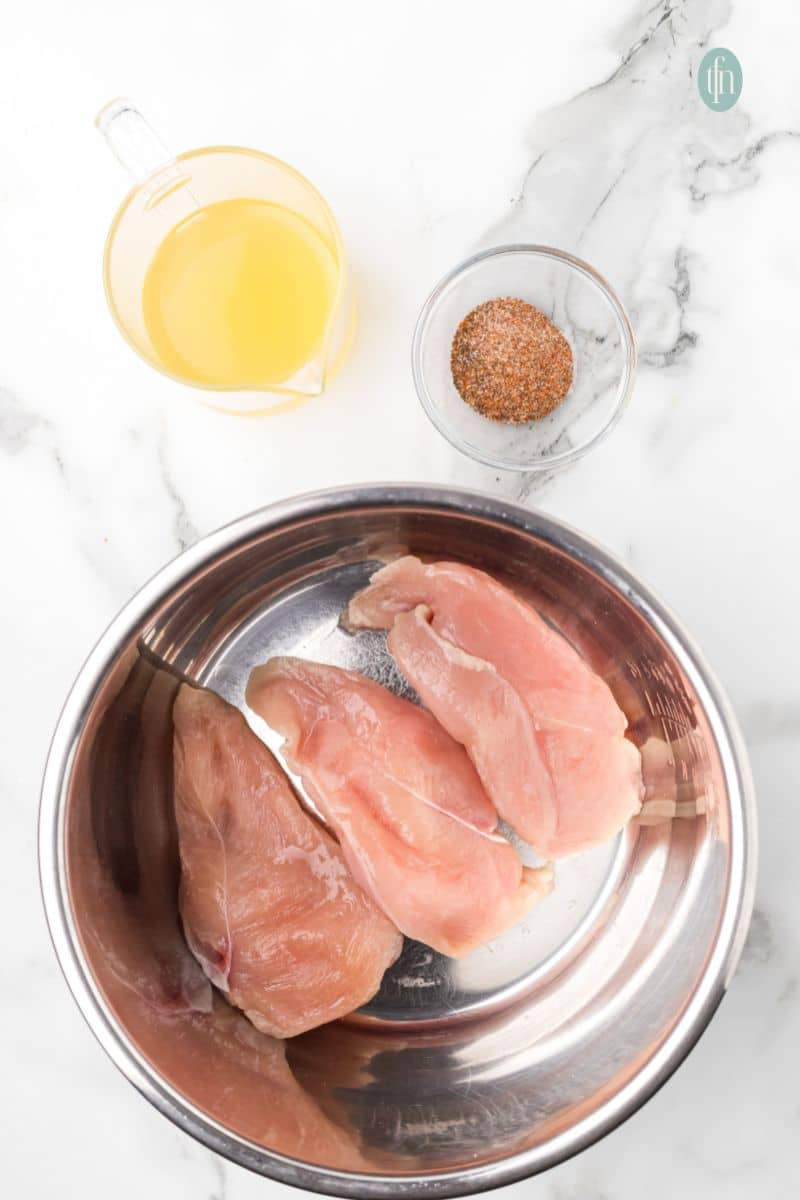A bowl with raw chicken and a bowl of seasoning plus a cup of chicken stock.
