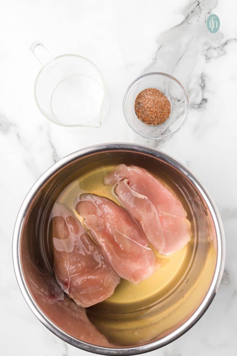 A bowl of raw chicken with liquid and a bowl of seasoning.