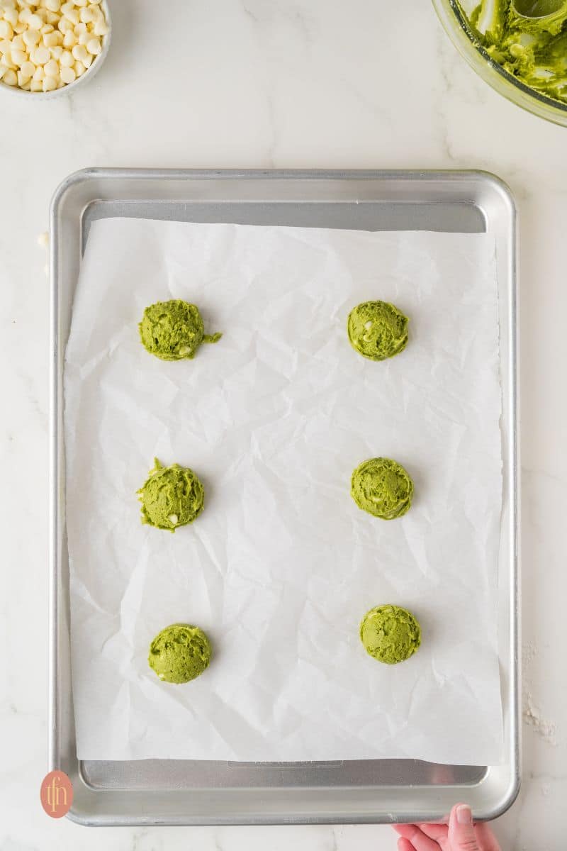 Six cookie balls on a baking pan with parchment paper.