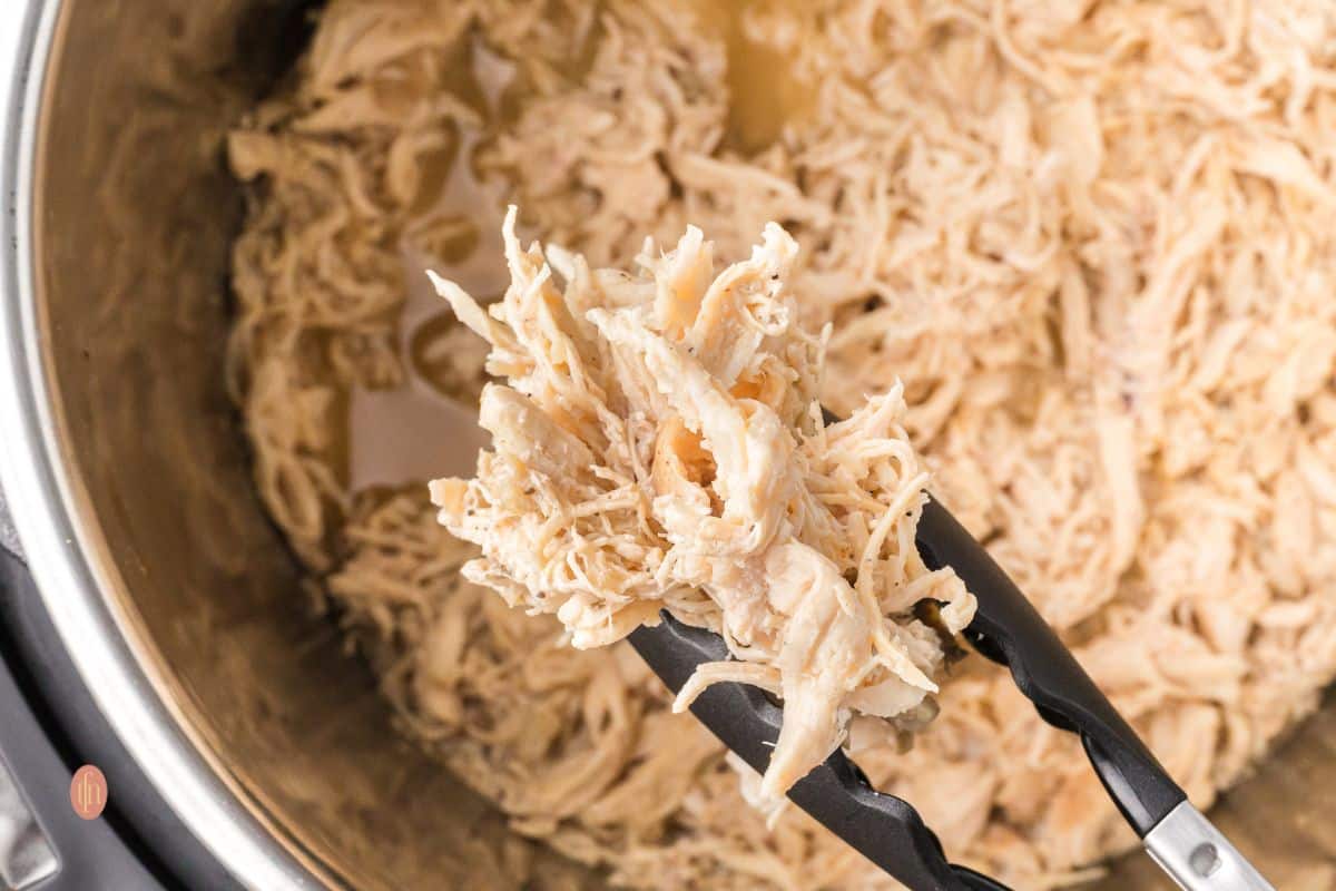 Shredded chicken in an Instant Pot with tong.