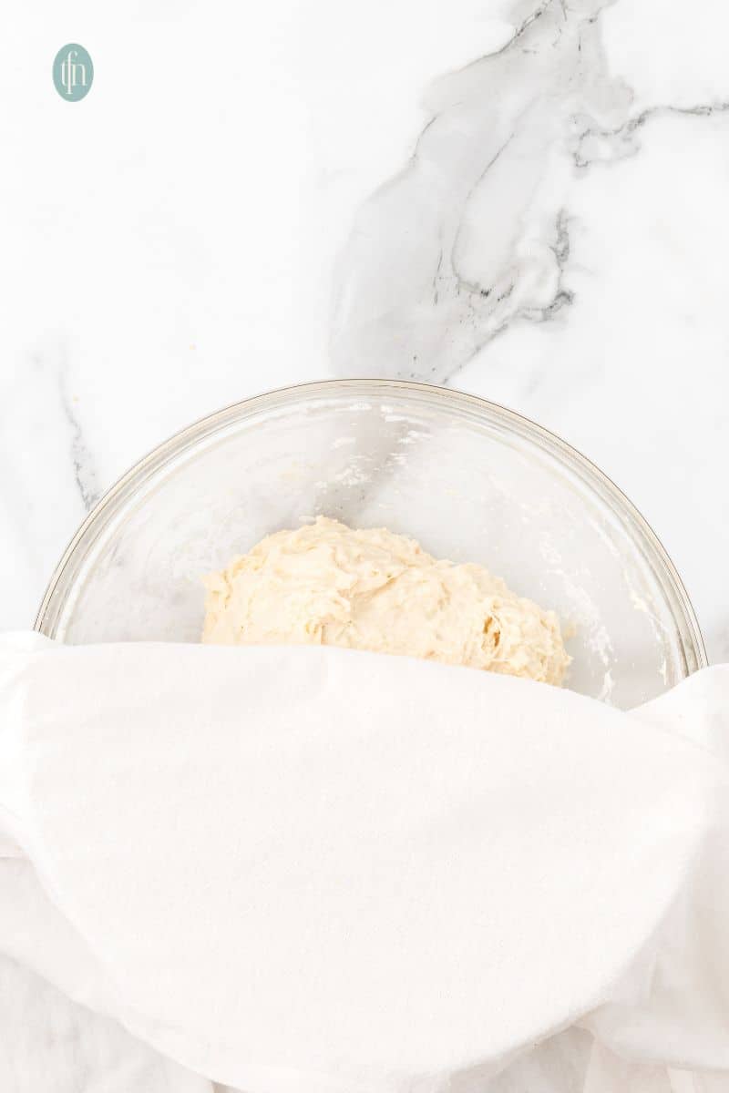 A glass bowl with dough covered with cloth.