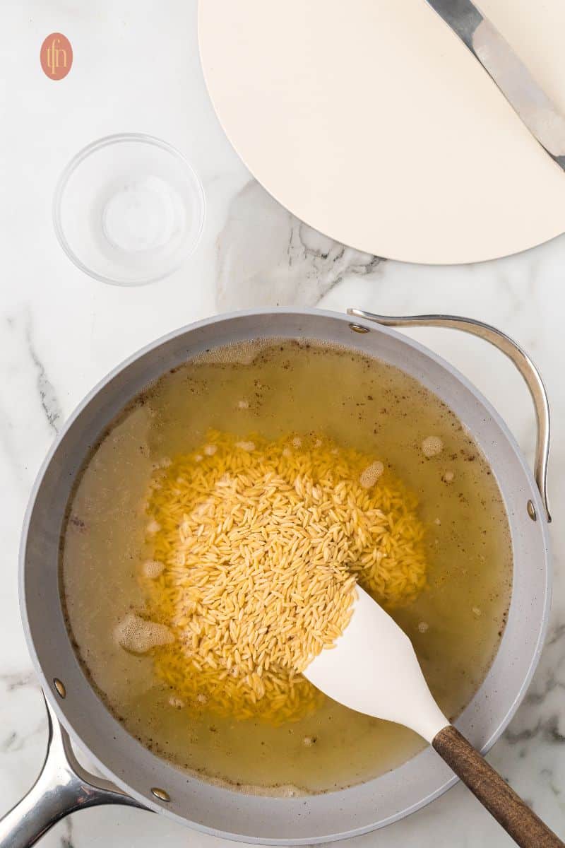 A pan of liquid mixture with orzo.
