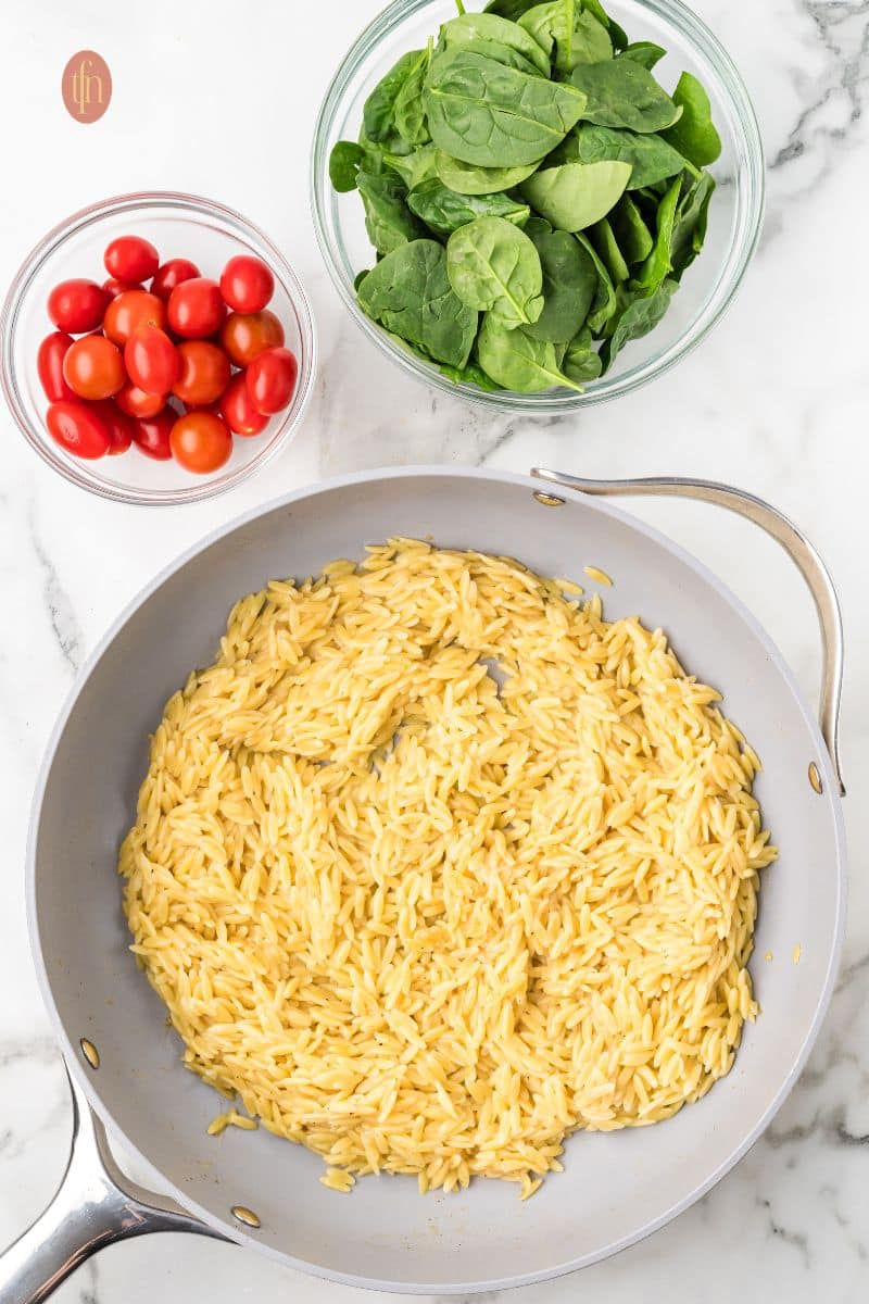 A pan of orzo and a bowl of tomatoes and greens.