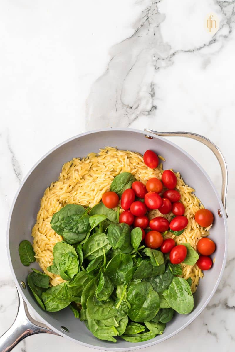 A pan of orzo with tomatoes and green leafy vegetables.