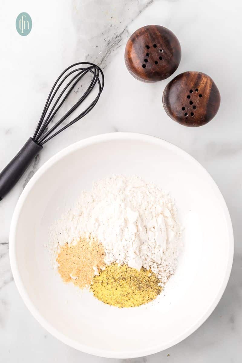 A bowl of powdered ingredients, salt and pepper shaker, and a whisk.